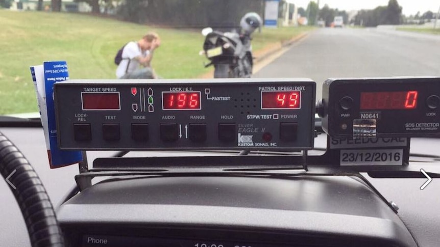 Police radar speed with motorcyclist with head in his hands on the grass outside the police car