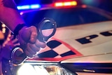 Male police officer's hand holding a set of handcuffs in front of a police car.