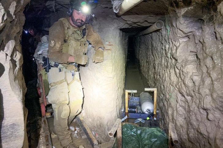 A man stands to the left of the image in khaki protective gear. A second tunnel is to his left.