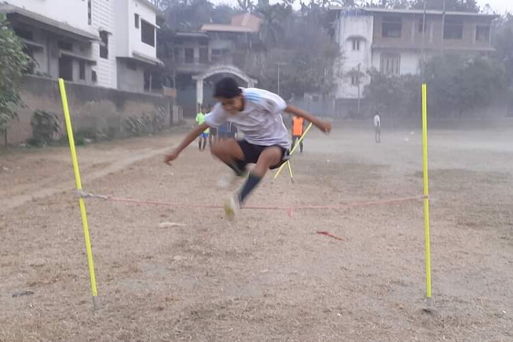 A girl jumps over a rope on a dusty sports field.