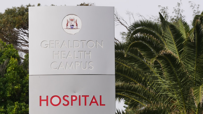 A grey sign with Geraldton Health Campus embossed on it. Below is red text saying hospital. There are palm trees behind it.  