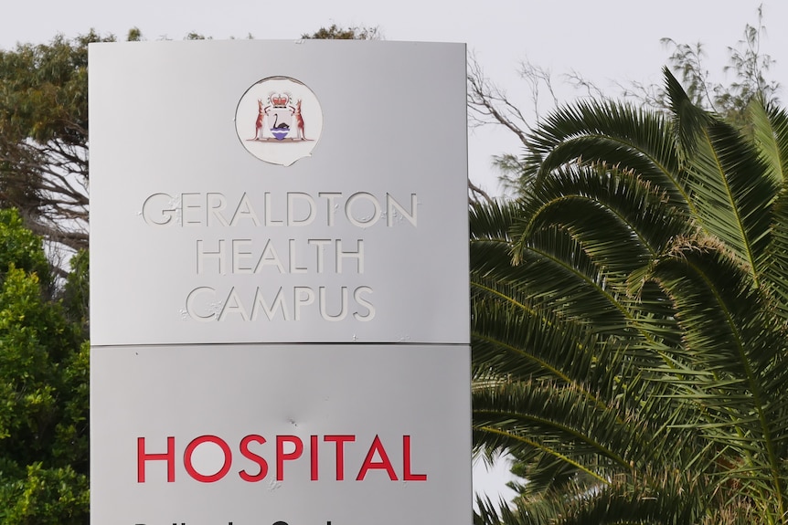 A grey sign with Geraldton Health Campus embossed on it. Below is red text saying hospital. There are palm trees behind it.  