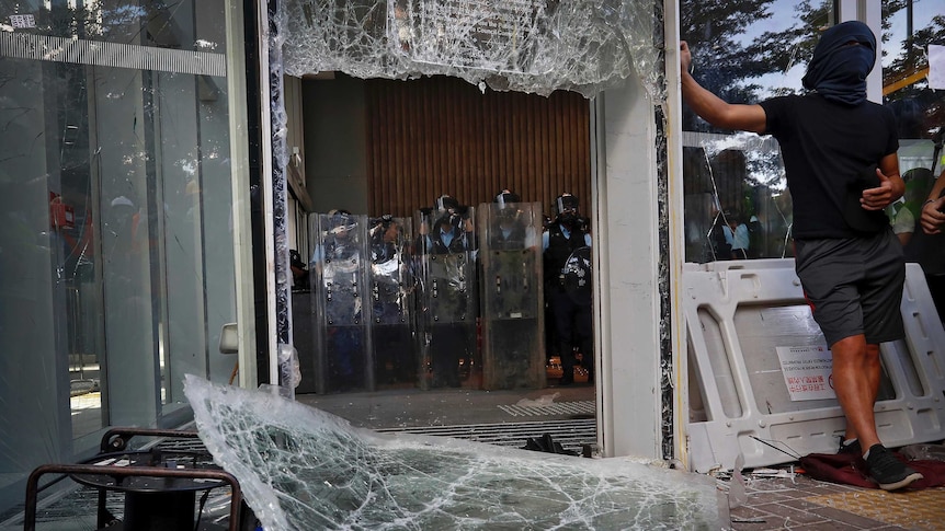 Police inside Hong Kong's Legislative Council stand back after protesters smash through windows.
