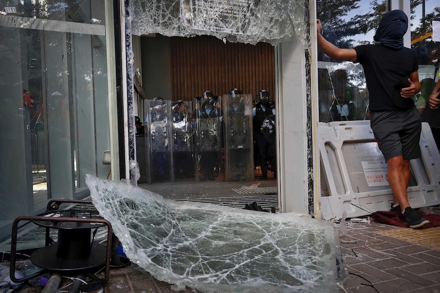 Police inside Hong Kong's Legislative Council stand back after protesters smash through windows.