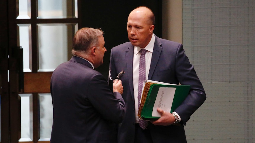 Mr Albanese and Mr Dutton are in discussion, near the doors of the House of Representatives chamber. Mr Dutton is holding notes.