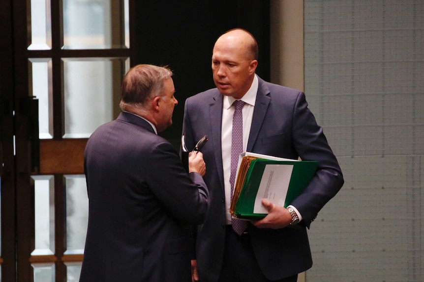 Mr Albanese and Mr Dutton are in discussion, near the doors of the House of Representatives chamber. Mr Dutton is holding notes.