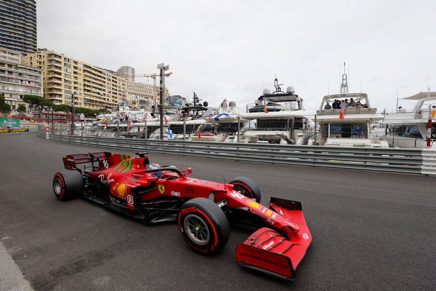 Red F1 car drives past a harbour filled with boats.