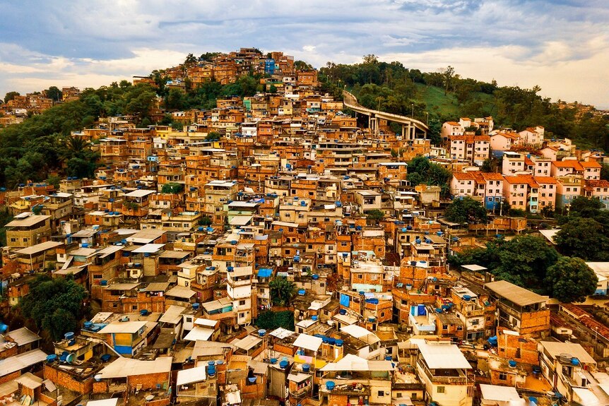 A sprawling favela of dense houses dominate the side of a hill but pockets of trees and grass remain