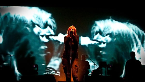 Beth Gibbons sings into a mic centrestage. Trippy visuals play on screens behind her.