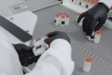 Inside a lab gloved hands are handling bottles of drugs