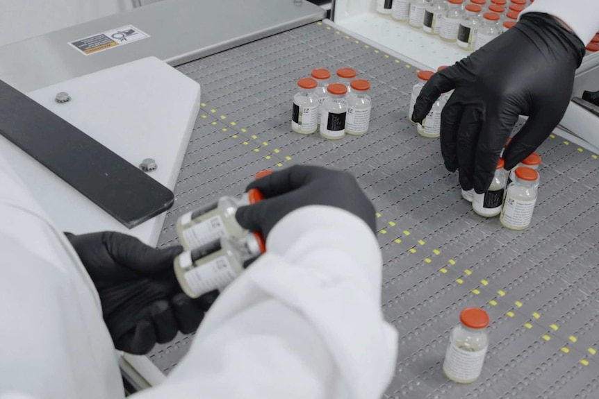 Inside a lab gloved hands are handling bottles of drugs
