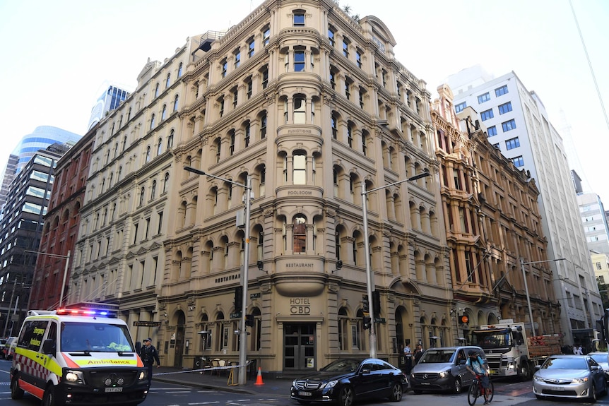 A building is seen on the corner of the street with an ambulance on the left hand side and cars waiting to the right.