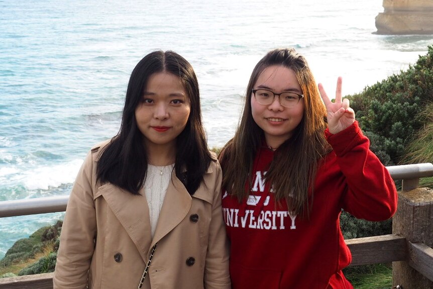Two Chinese university students pose for a photo by the ocean.