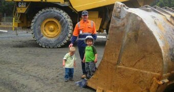 A man and two children stand beside heavy earthmoving machinery