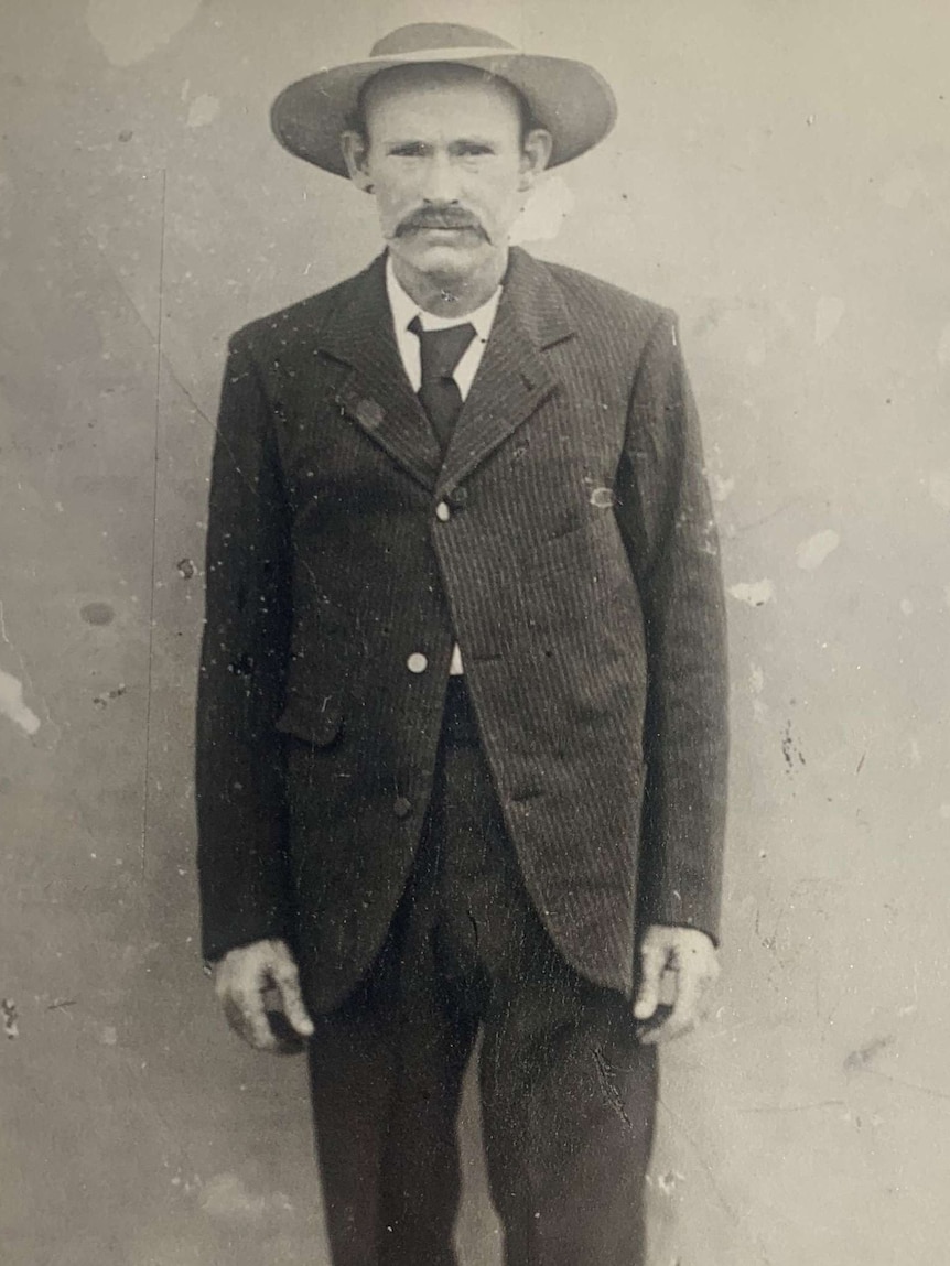 black and white portrait of a tall young moustached man wearing a suit and a brimmed hat.