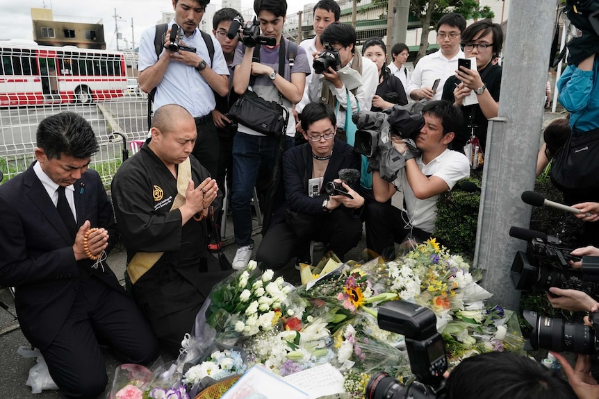 A group of media pray in front of flowers, with a large number of media filming them
