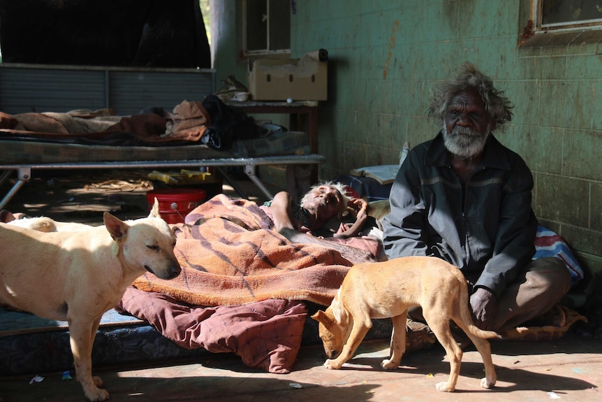 Kathleen Ngale and her husband Motorbike Paddy Ngale sit on a mattress with two dogs.