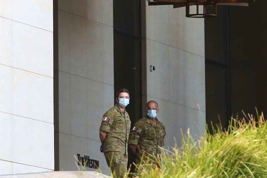 Two ADF personnel wearing face masks stand near the entrance to the Westin Hotel in Perth.