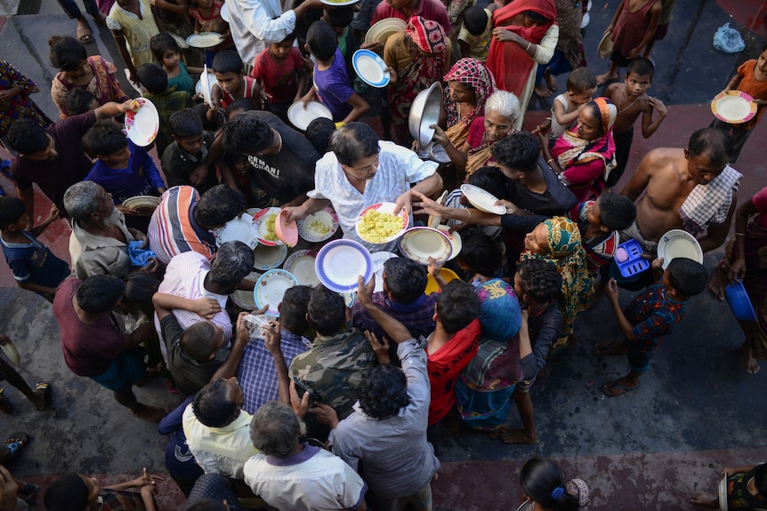 A shot from above shows people crowding around a man handing out plates of food