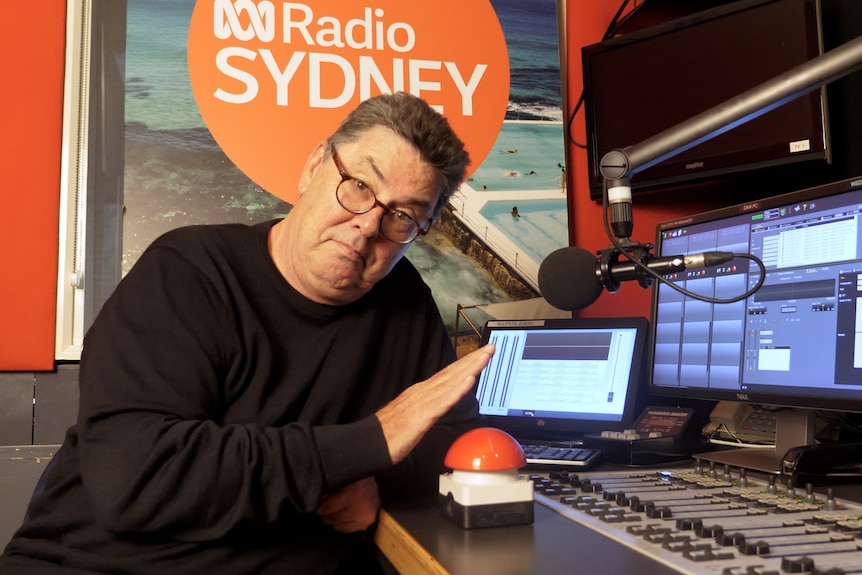 A man in a studio with his hand hovering over a red button. 