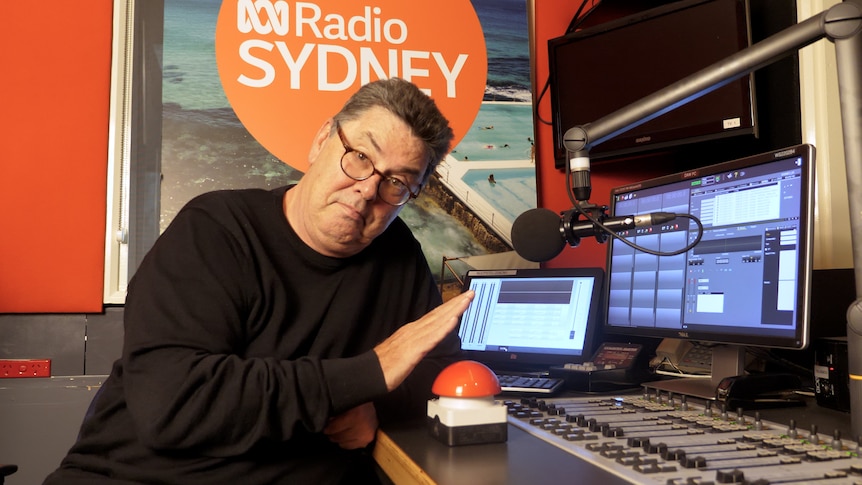 A man in a studio with his hand hovering over a red button. 