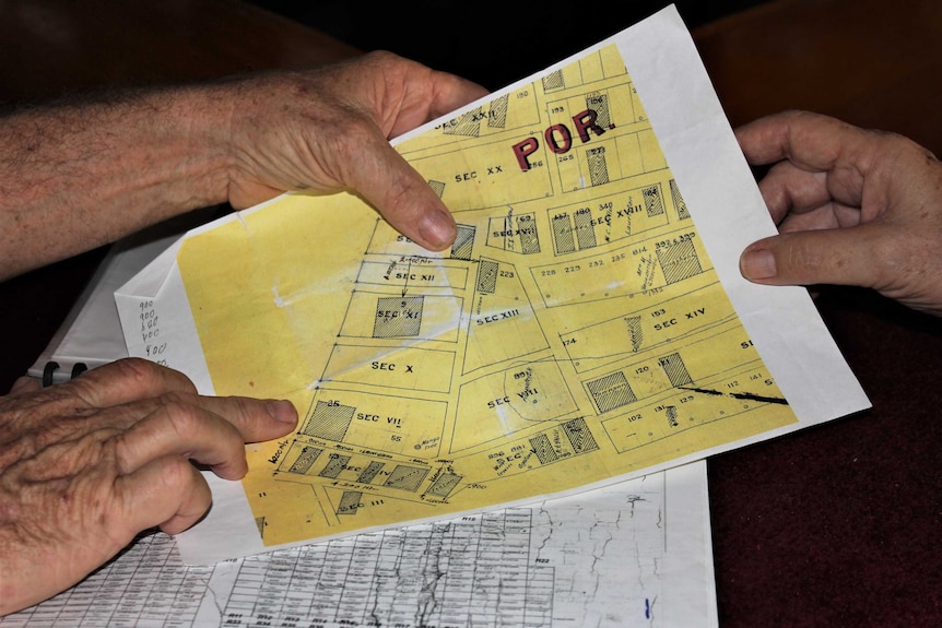 Hands point at a yellow map showing burial plots at a cemetery.