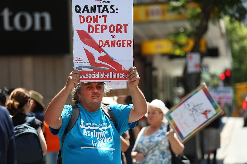 A protester outside the Qantas AGM in Brisbane wearing a t-shirt supporting asylum seekers and holding a sign.