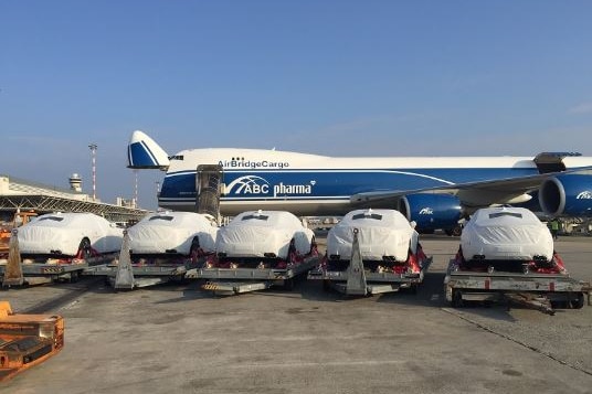 A row of cars covered in a white material are lined up in front of a plane.