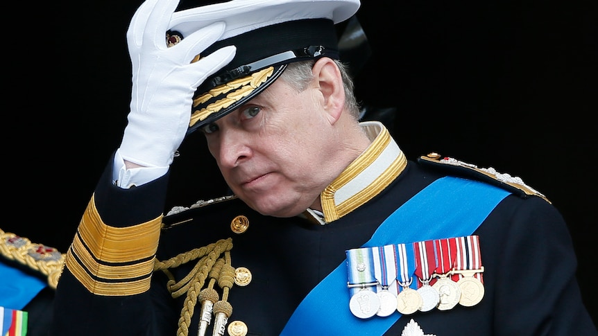 Prince Andrew touches his military hat and looks at the camera.