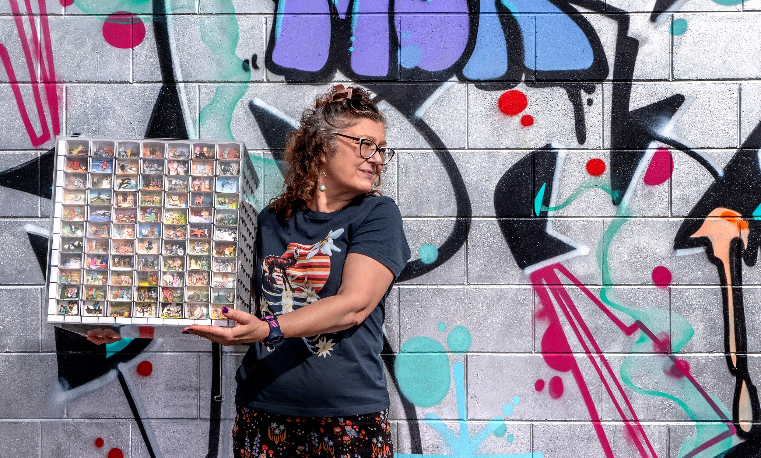 A woman holds a large box that is an artwork featuring matchboxes with miniature collages.