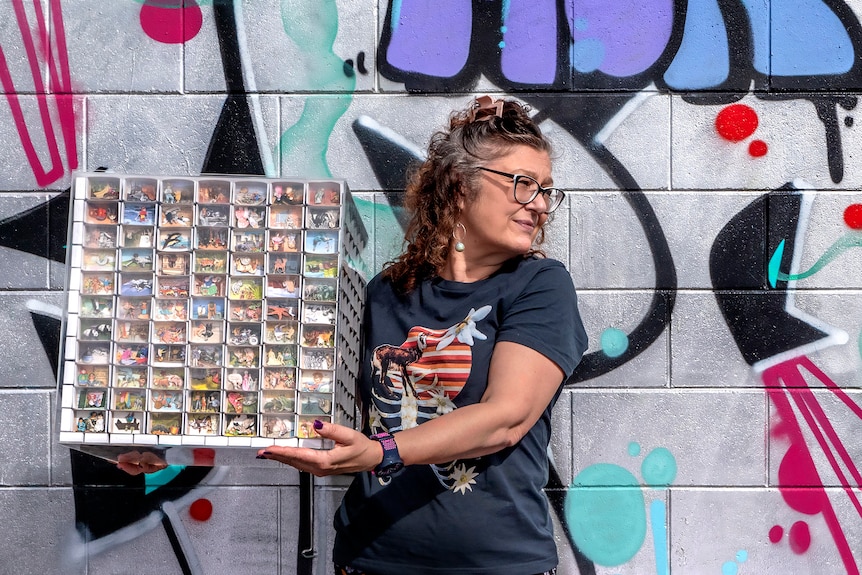 A woman holds a large box that is a work of art with matchboxes with miniature collages.