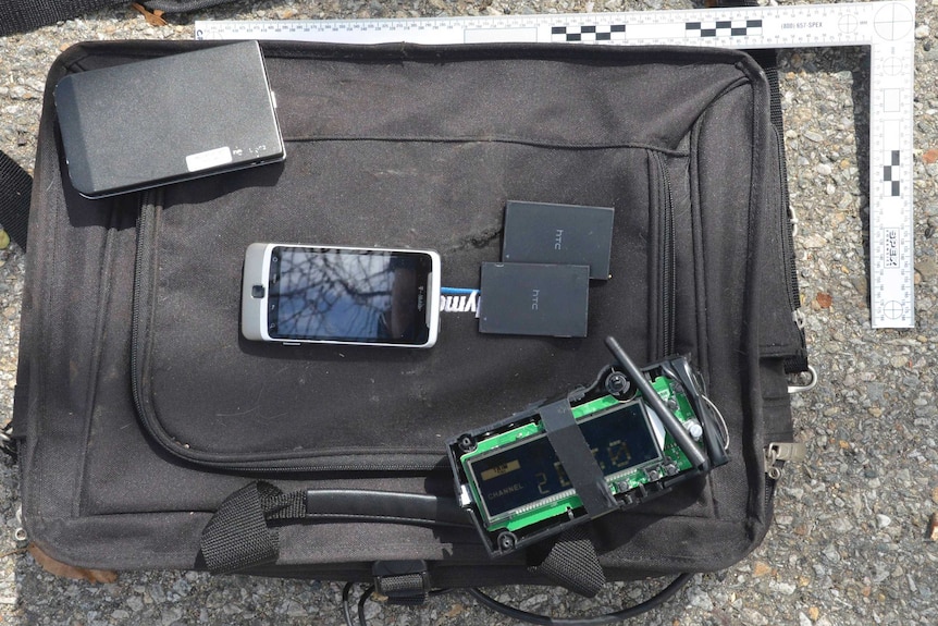A black laptop case, portable hard drive, cell phone, and a homemade remote control device.