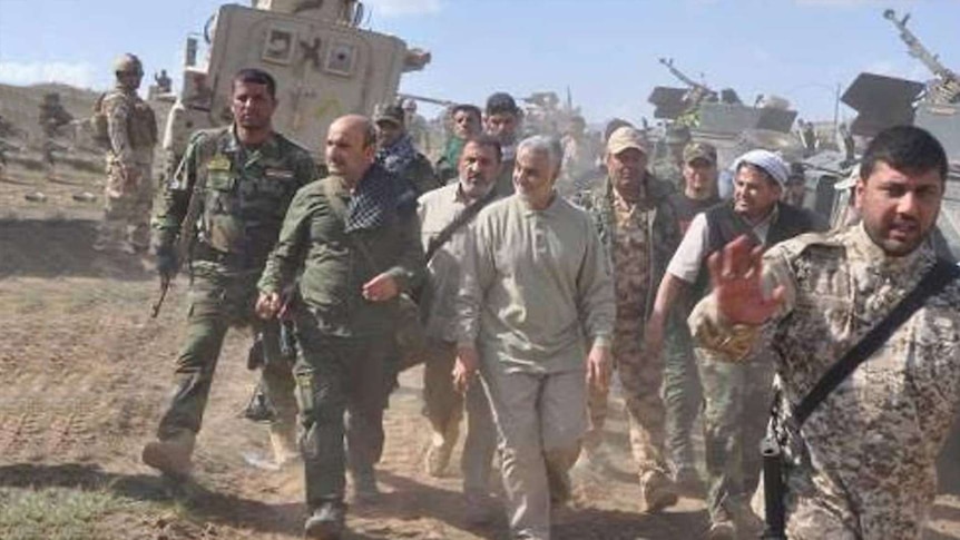 Qassam Soleimani walks with military members along a sandy road