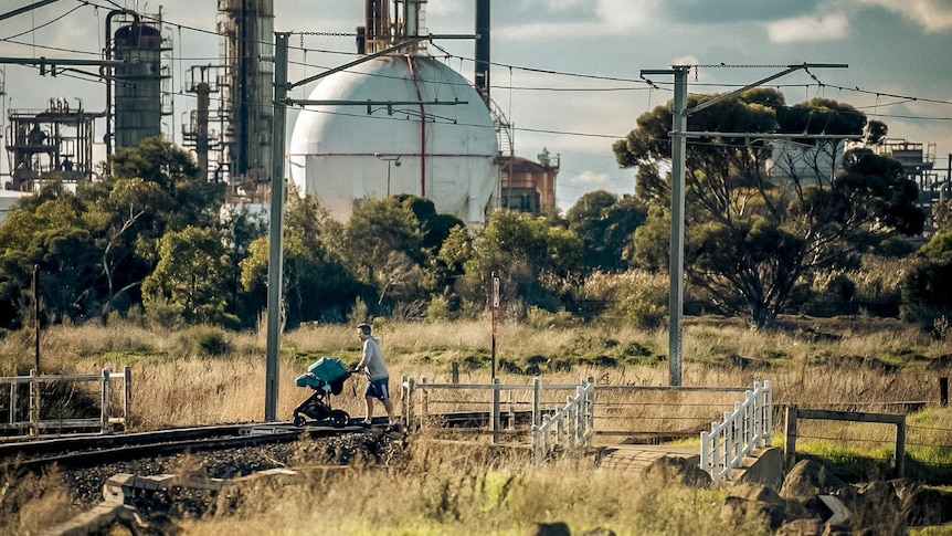 A man walks across a train track, in front of the Altona Oil Refinery site