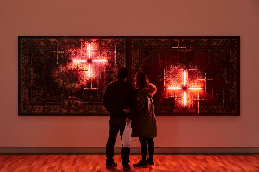 Colour image of two people looking at Norberto Roldan's mixed media artwork 'Crusade' in the Art Gallery of New South Wales.