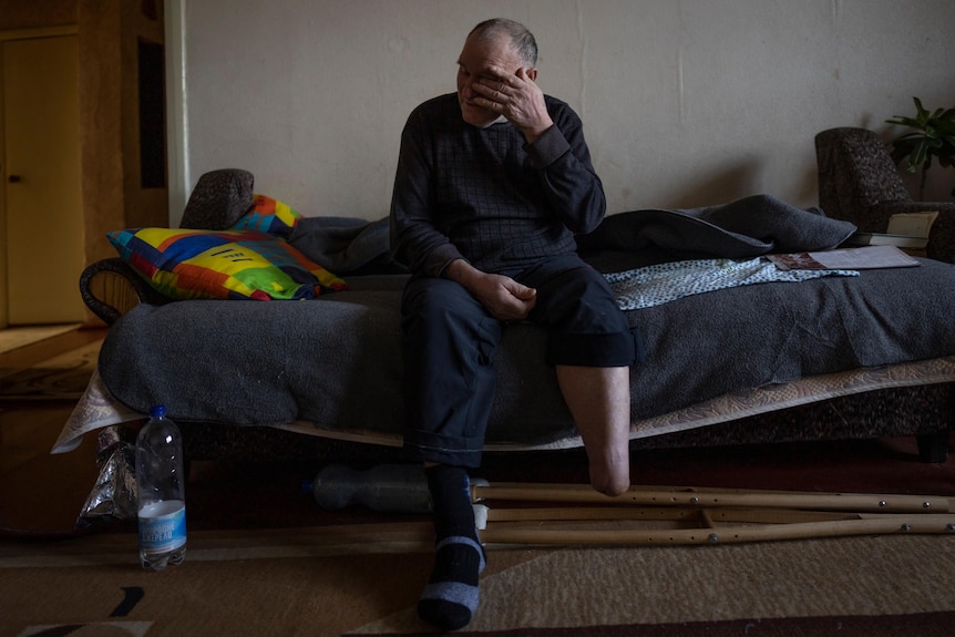 Land mine victim Vasily Hrushka sits on a bed and wipes his eye 
