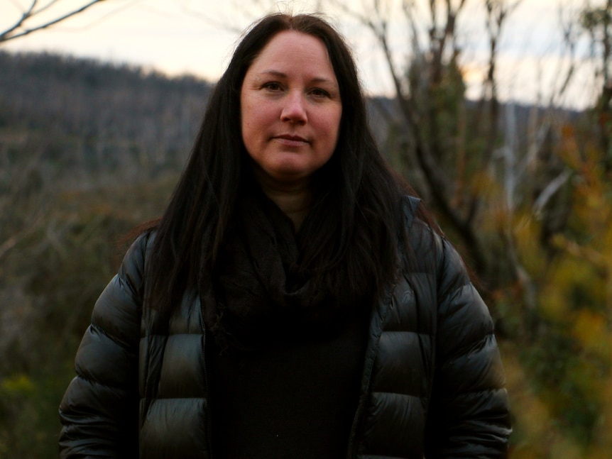 Volunteer Kat Boehringer stands in the centre of a shot, with burnt bushland behind her.