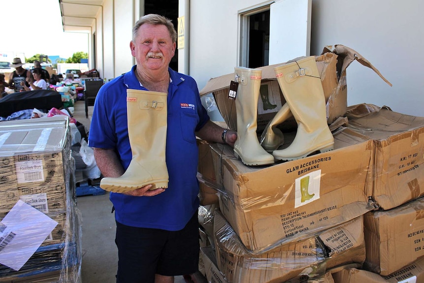 Food Relief NQ warehouse supervisor Toby Kelly stands next to a pallet of gumboots.