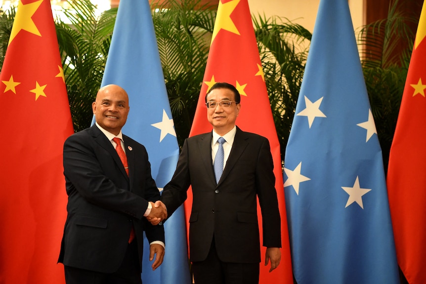 Two men in suits smile as they shake hands before the flags of Micronesia and China at an official event.