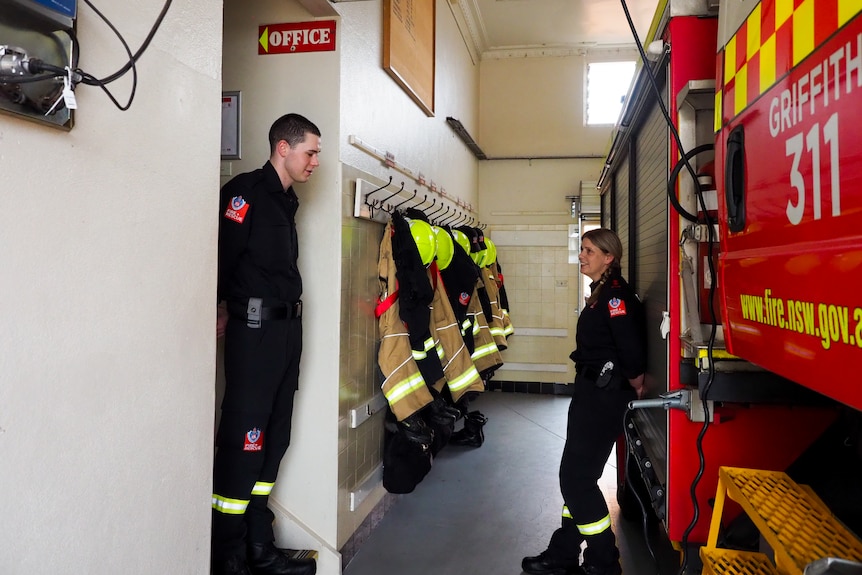 Captain Danielle McKay leans on a fire truck talking to another fire fighter