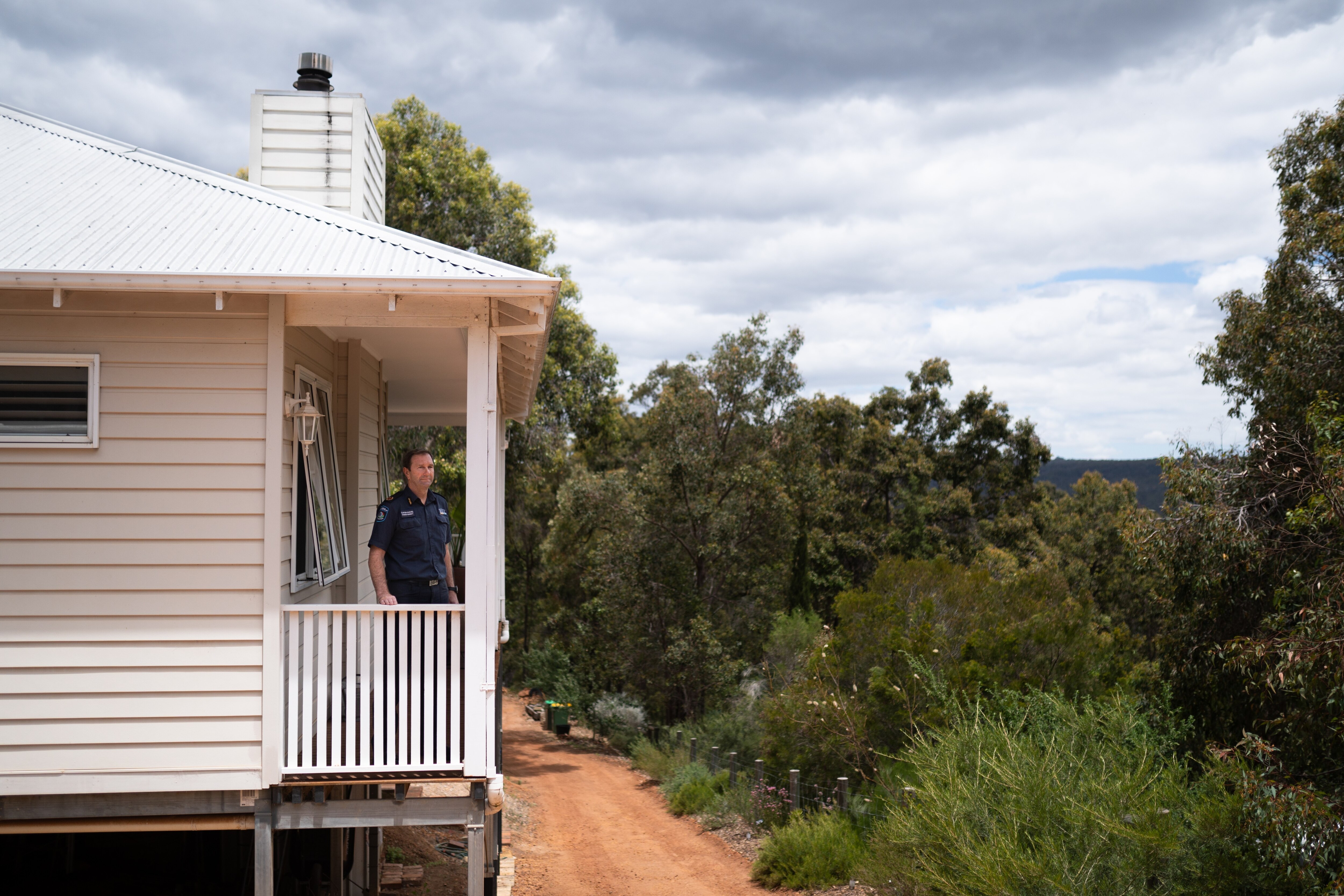 Retrato de um homem parado em sua varanda com vista para a mata australiana em seu quintal