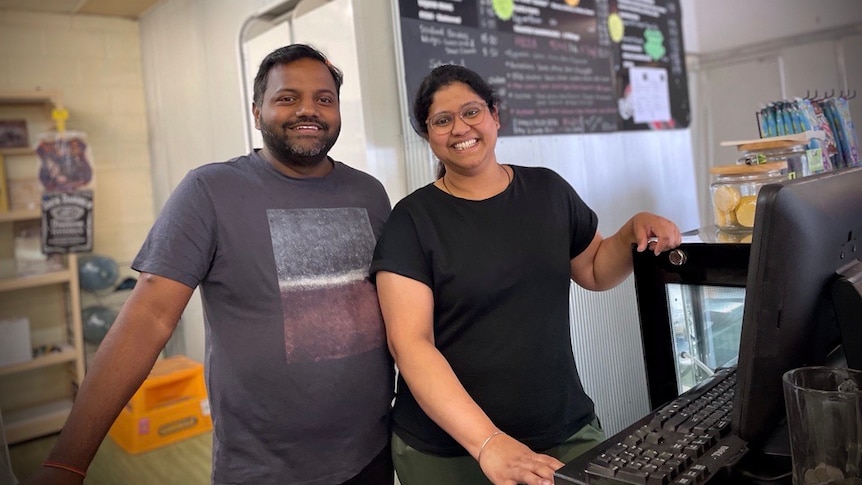 Satish and Priti Tati, two people standing behind a cash register and computer, they are smiling.