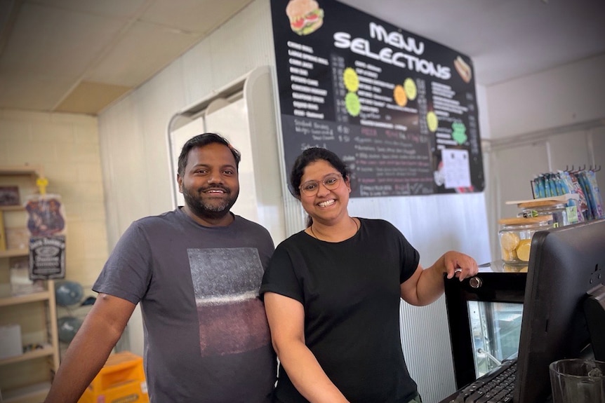 Satish and Priti Tati, two people standing behind a cash register and computer, they are smiling.