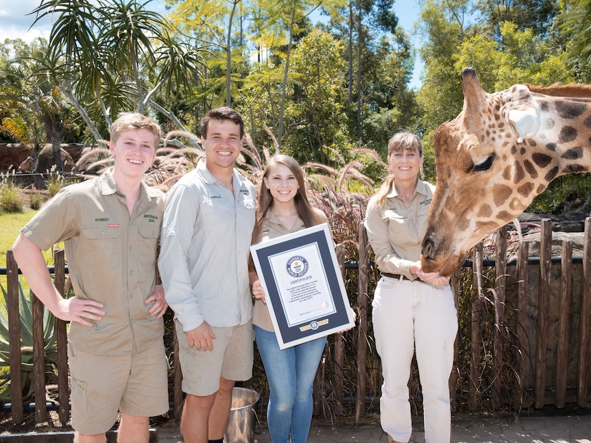 Four people holding an award next to a large giraffe, outdoors.