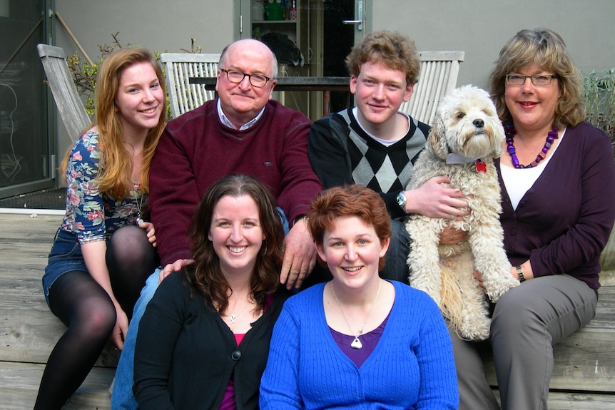 Six members of a family holding a dog while smiling at the camera