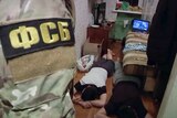 Two men lying on the floor in a bedroom as security forces stand at the door.