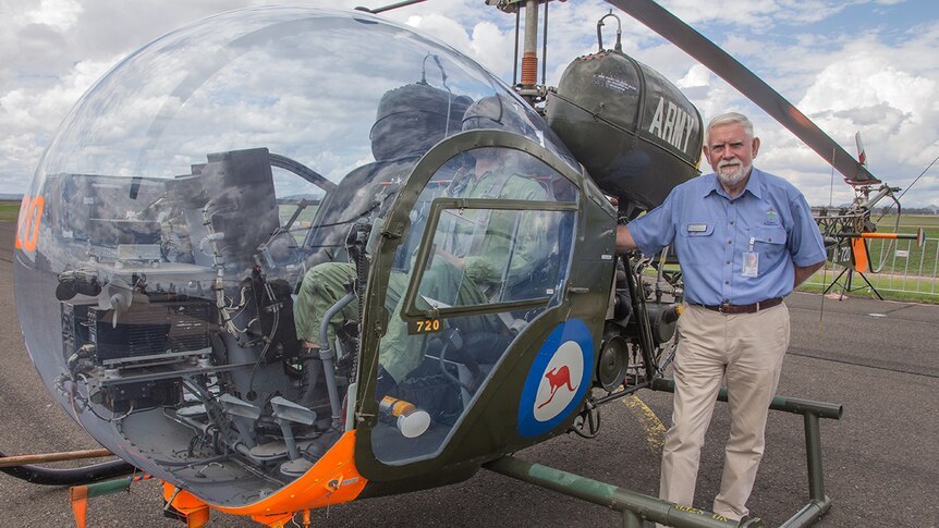 A man stands in front of an Army Bell 47 helicopter