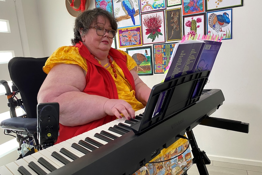 Woman wearing yellow and red top playing a keyboard. 