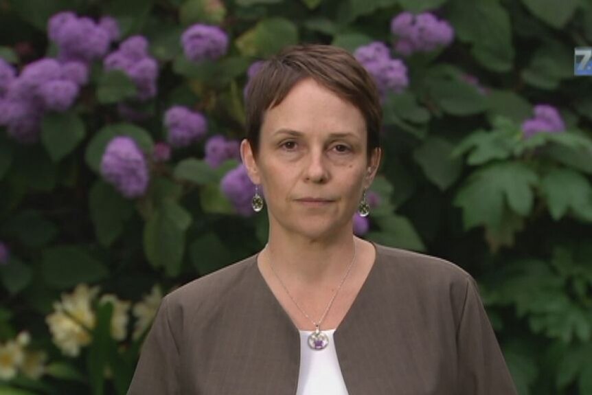 A middle-aged woman with a pixie-style hair cut stands in front of what appears to be a wisteria bush.