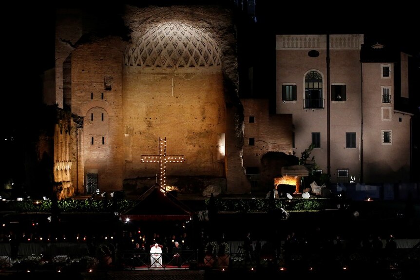 A wide shot shows the Pope sitting on a lit stage in front of a large crowd